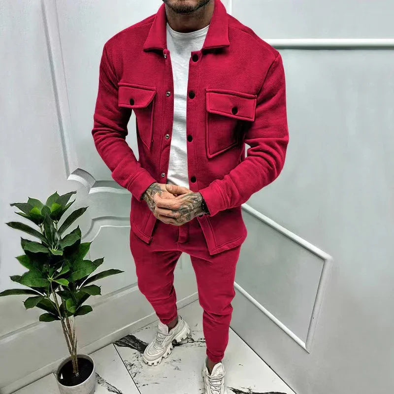 Man wearing a red jacket and matching red joggers with white sneakers standing indoors next to a potted plant