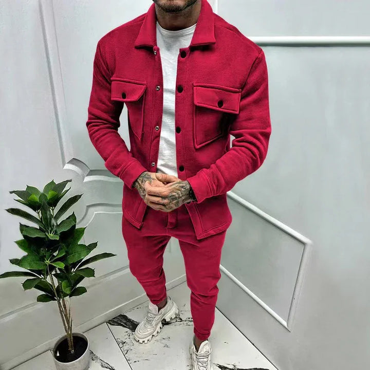 Man wearing a red jacket and matching red joggers with white sneakers standing indoors next to a potted plant