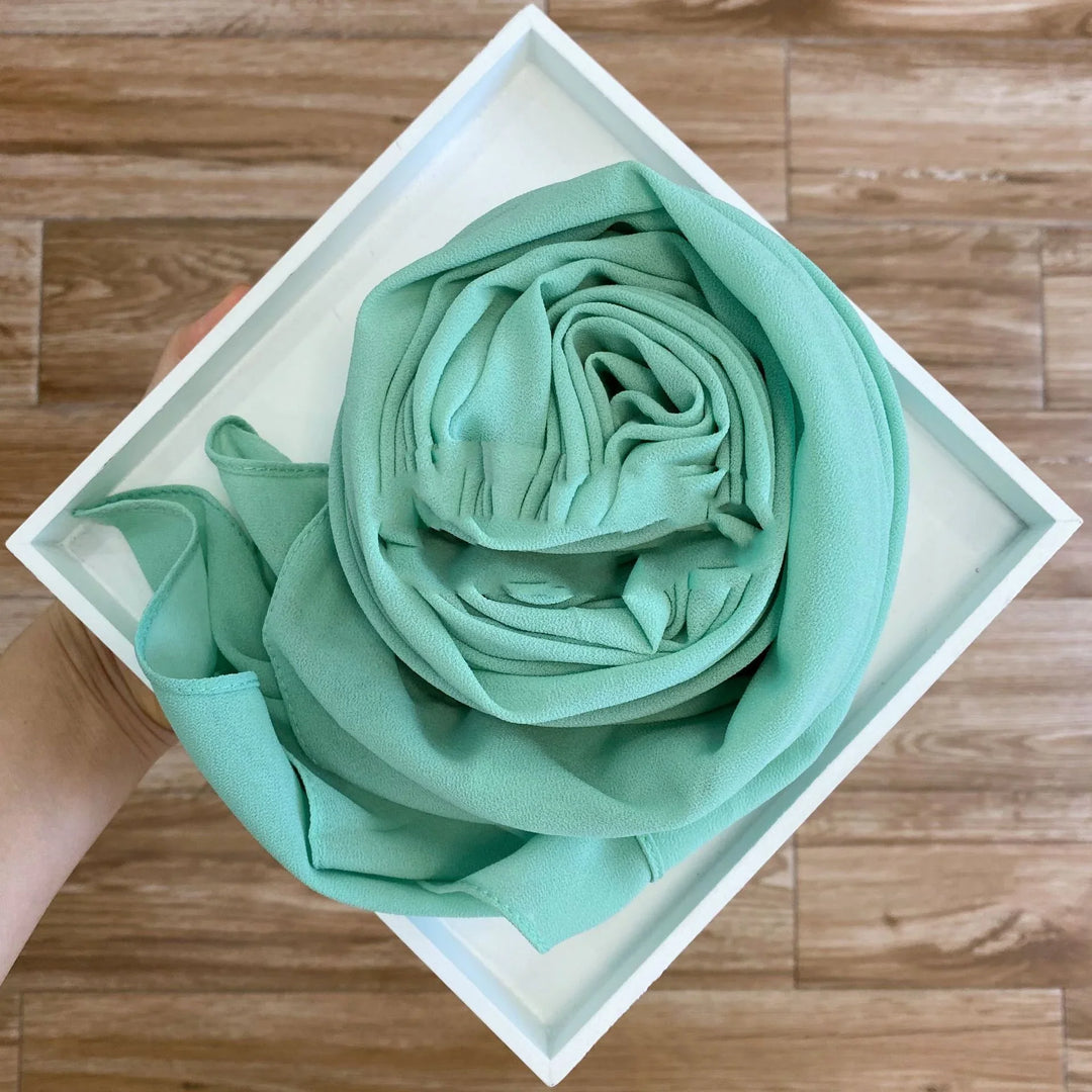 Hand holding a white tray with a neatly rolled mint green fabric scarf on wooden floor