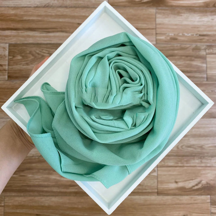 Hand holding a white tray with a neatly rolled mint green fabric scarf on wooden floor