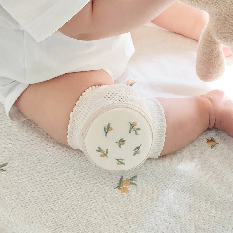 Baby wearing white knit knee pads with yellow floral design on a white floral blanket