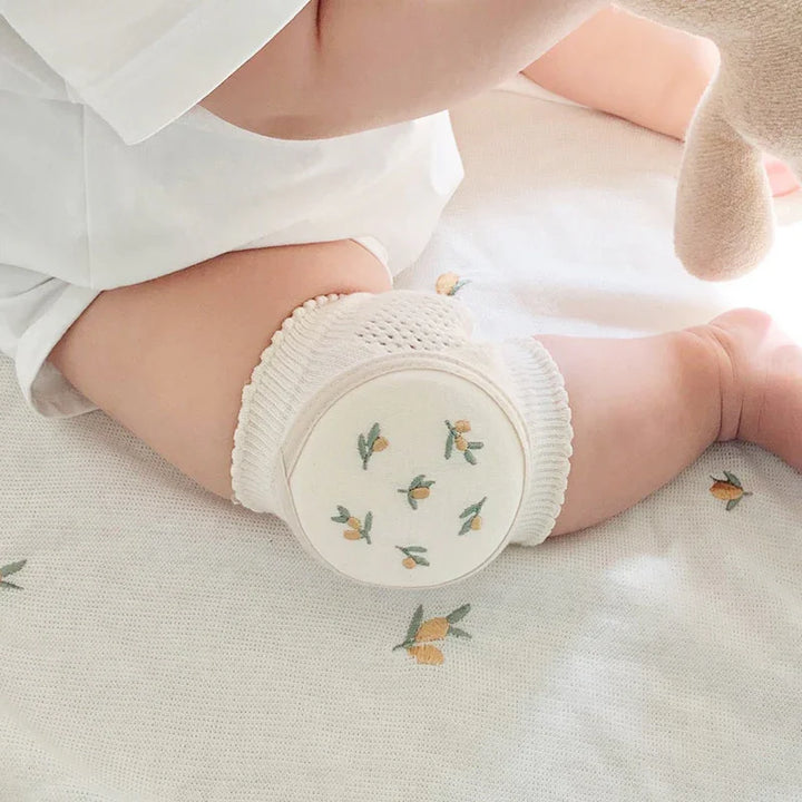 Baby wearing white knit knee pads with yellow floral design on a white floral blanket