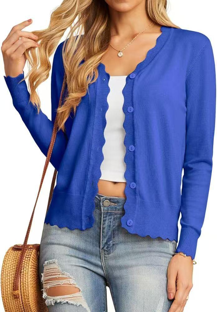 Woman wearing a blue scalloped edge button-up cardigan, white crop top, distressed jeans, and carrying a round straw bag