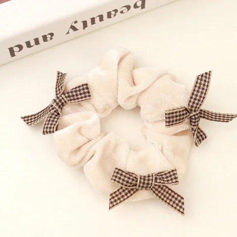 Cream-colored velvet hair scrunchie with three brown checkered ribbon bows on white background
