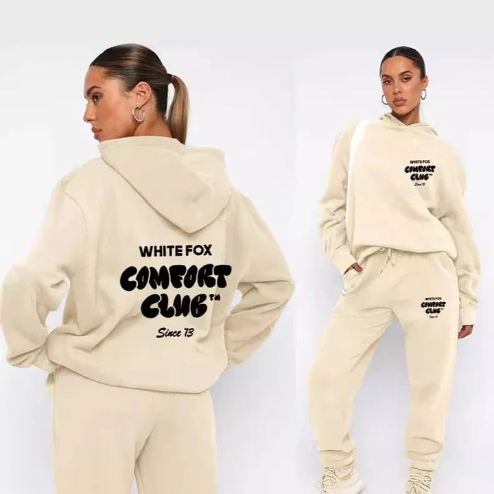 Woman wearing beige White Fox Comfort Club hoodie and joggers loungewear set with black text, styled with hoop earrings and sneakers