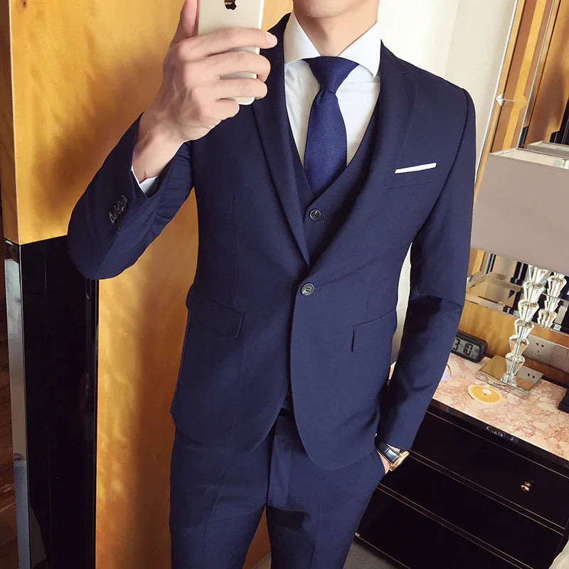 Man wearing a fitted navy blue three-piece suit with a white dress shirt and navy tie taking a mirror selfie