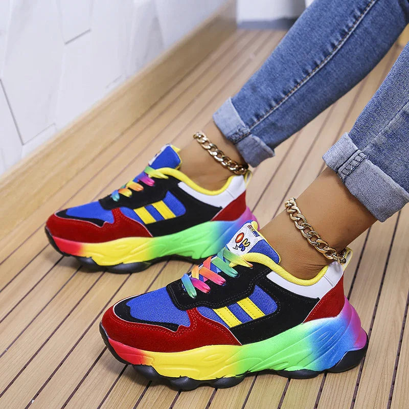 Colorful chunky sneakers with gradient rainbow soles worn with rolled-up blue jeans and gold anklets