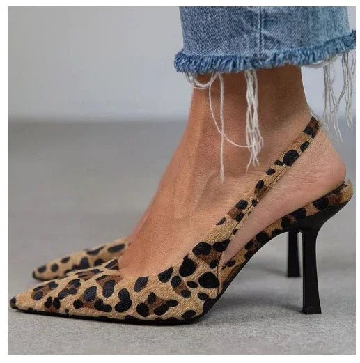 Close-up of leopard print slingback high heels worn with frayed hem denim jeans on gray floor