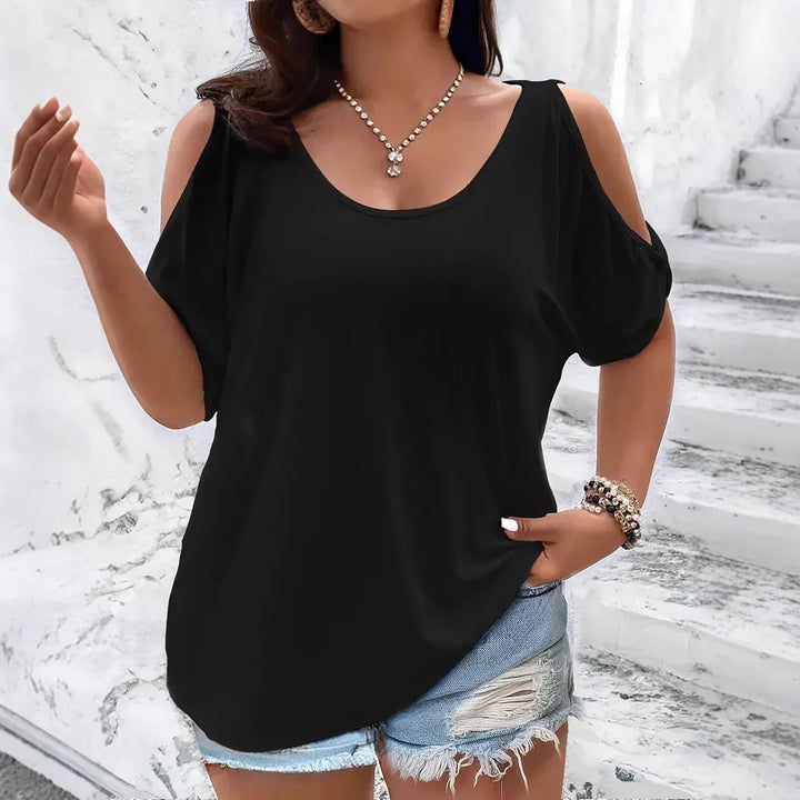 Woman wearing black cold shoulder top paired with distressed denim shorts in front of marble stairs