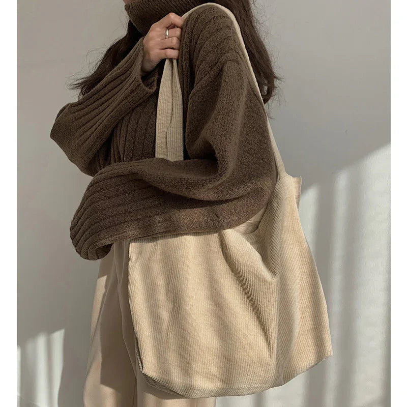 Woman wearing brown ribbed sweater holding beige corduroy tote bag in soft natural light