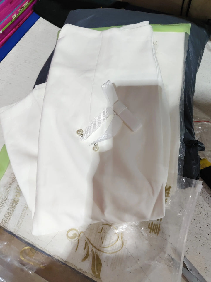 White folded fabric with two pearl-adorned white ribbon pins on a cluttered surface