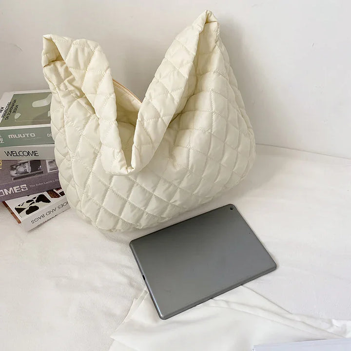 Cream quilted fabric tote bag with soft texture beside gray tablet and stacked books on white surface