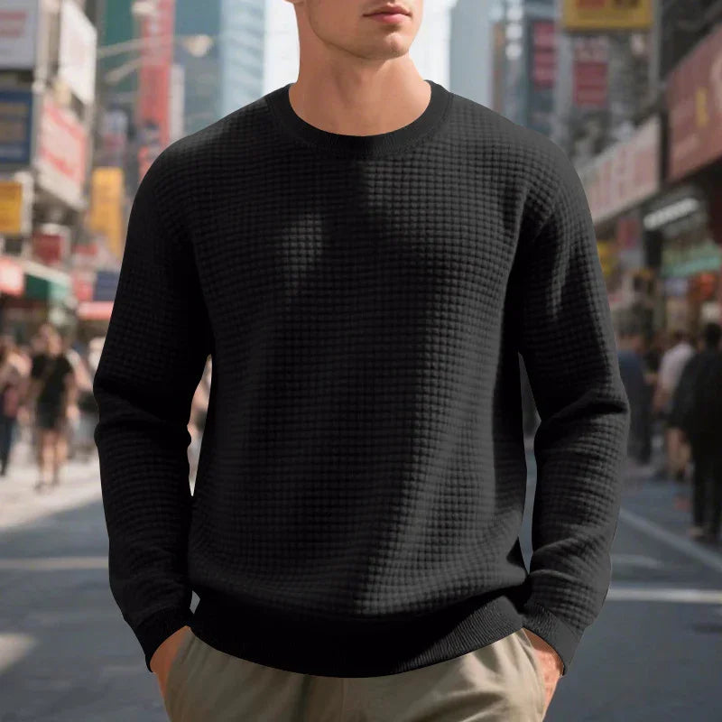 Man wearing black textured long sleeve sweater and beige pants in busy urban street