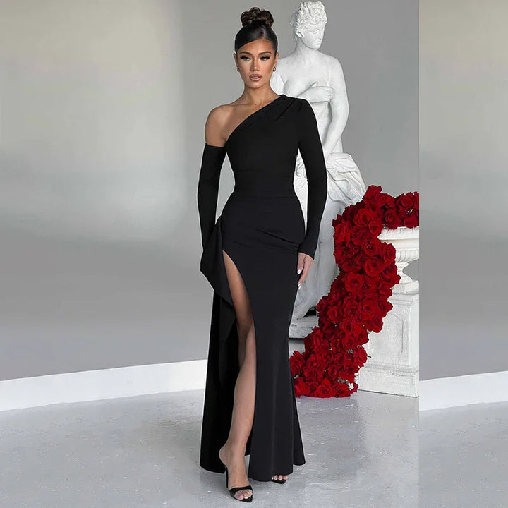 Elegant woman in a black one-shoulder gown with thigh slit poses by white statue and red roses
