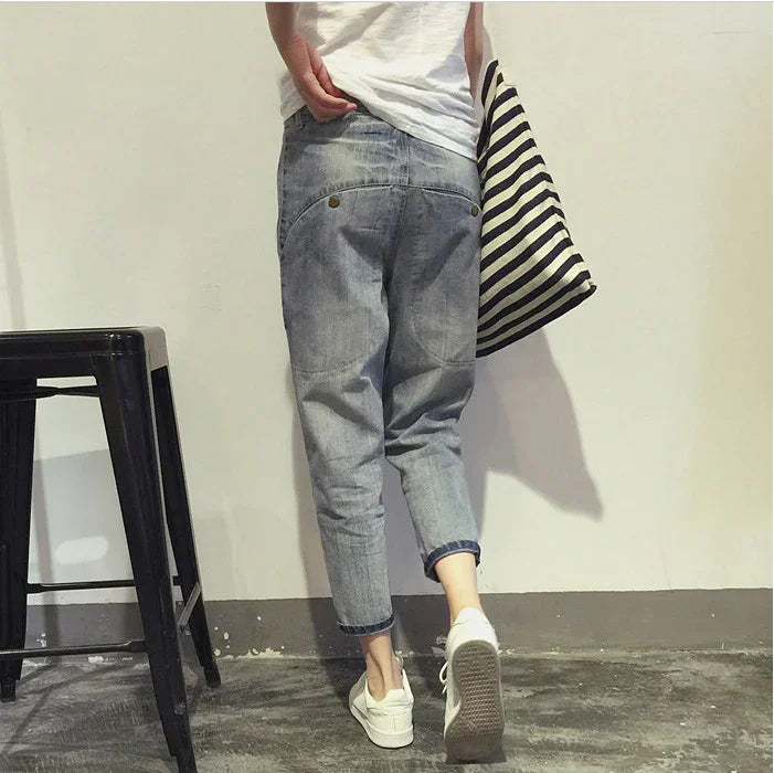 Person wearing rolled-up light blue denim jeans and white sneakers holding a striped tote bag