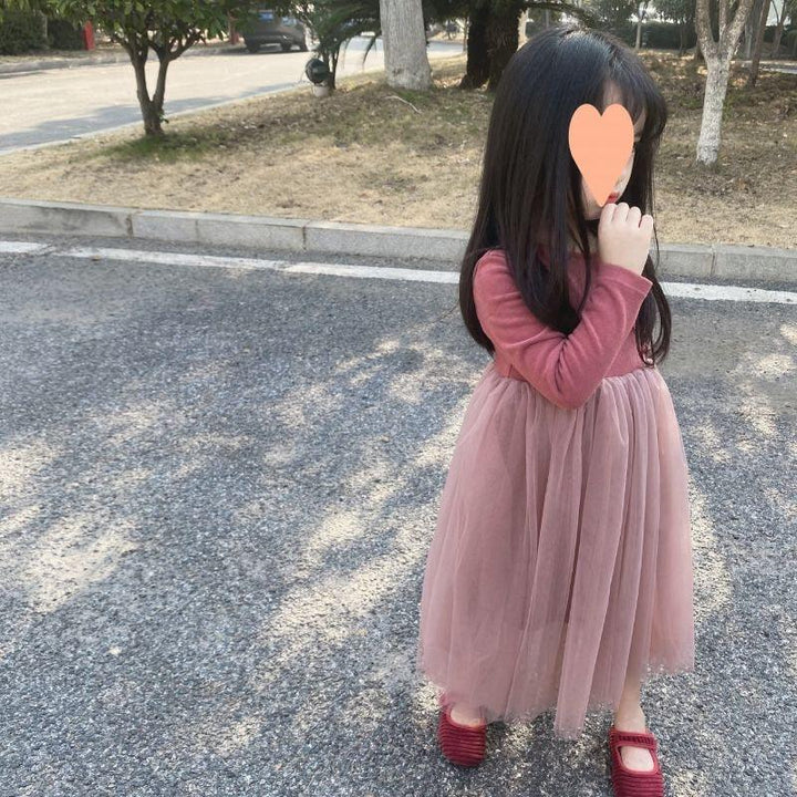 young girl in a pink long-sleeve top and tulle skirt standing on a paved road in a park