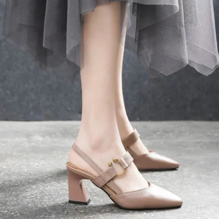 Woman wearing beige slingback block heel shoes with gold buckle detail on gray floor