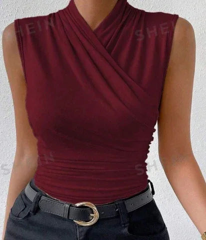 Woman wearing sleeveless burgundy wrap top paired with black belt and dark pants