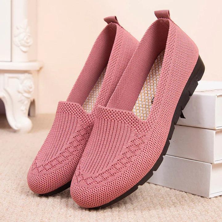 Pink knitted slip-on casual women's shoes with black soles placed on beige carpet near white boxes