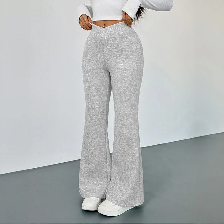Woman wearing high-waisted light gray flare pants and white sneakers against plain wall