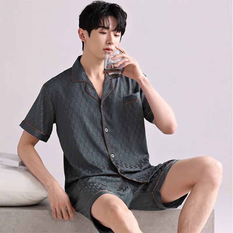 Man wearing dark patterned short-sleeve pajamas sitting and drinking from a glass