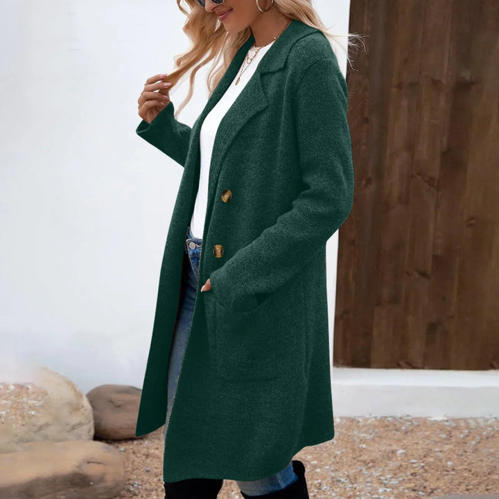 Woman wearing dark green woolen coat with gold buttons over white top and jeans outdoors