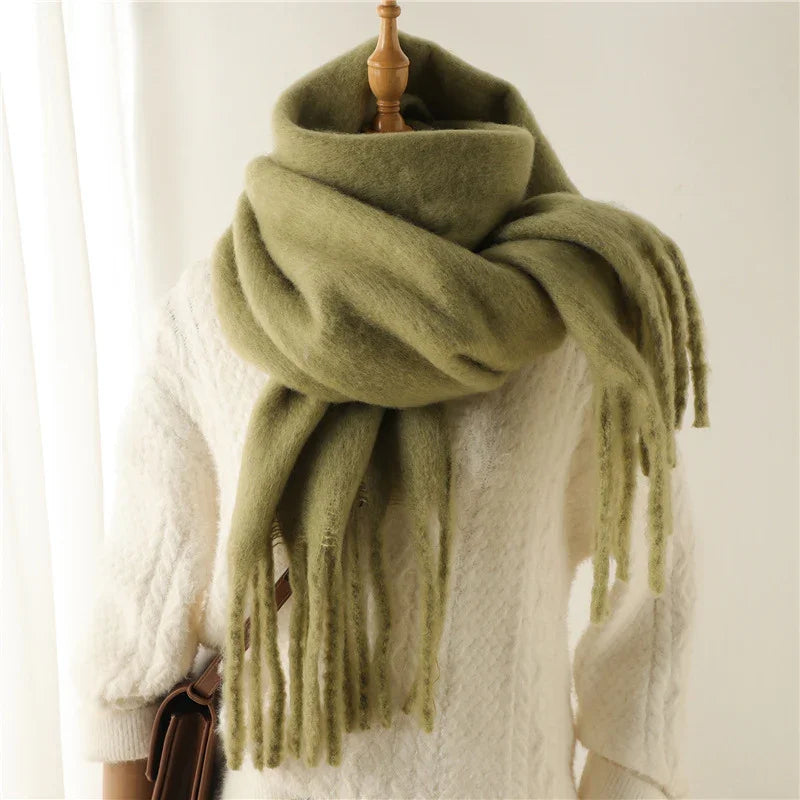 Soft olive green oversized scarf with fringe paired with a white cable knit sweater on mannequin