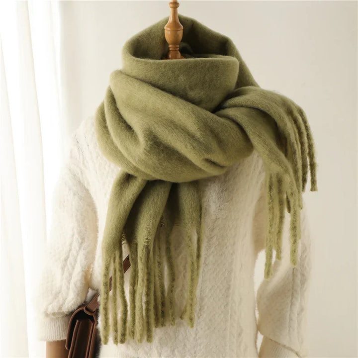 Soft olive green oversized scarf with fringe paired with a white cable knit sweater on mannequin