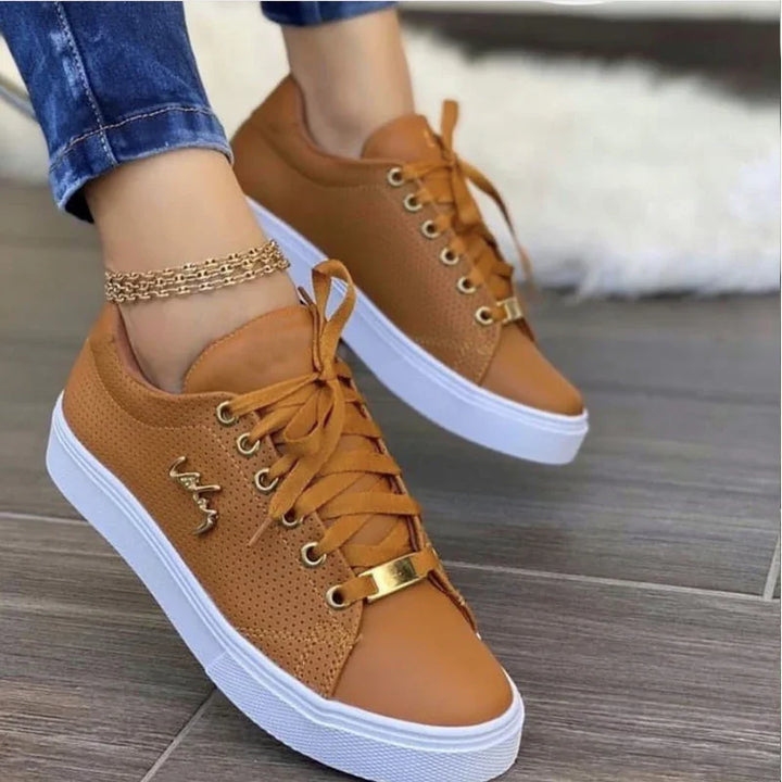 Tan leather sneakers with white soles and lace-up design worn with blue jeans on wooden floor