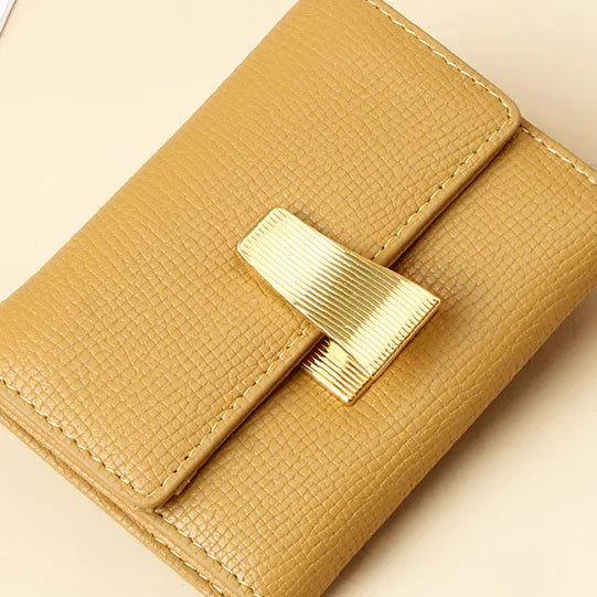 Small tan textured leather wallet with gold metal clasp on beige background