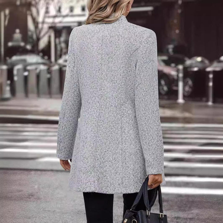 Woman wearing light gray herringbone blazer holding black handbag on city street