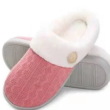 Pink knitted cozy slippers with white faux fur lining and beige button details on gray soles
