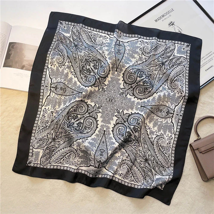 Elegant black and white paisley patterned silk scarf with decorative border, displayed flat on beige surface