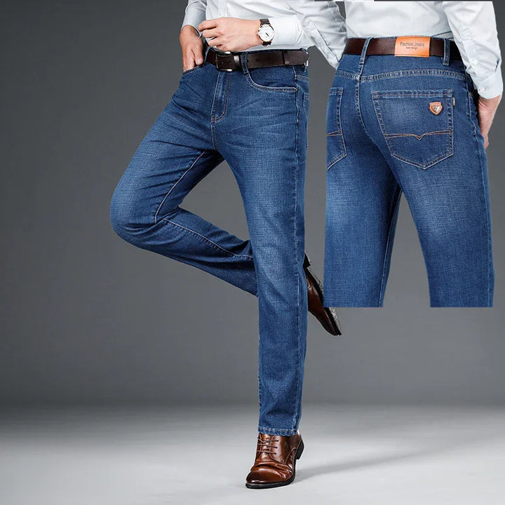 Men's slim-fit blue denim jeans styled with brown leather belt and matching brown dress shoes