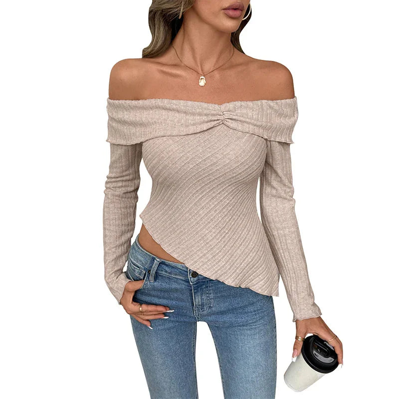 Woman wearing beige off-shoulder ribbed sweater with asymmetrical hem and blue jeans holding coffee cup