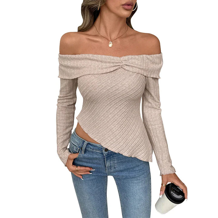 Woman wearing beige off-shoulder ribbed sweater with asymmetrical hem and blue jeans holding coffee cup