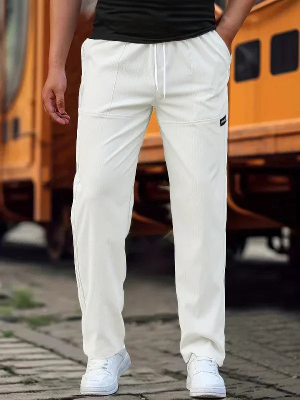 Man wearing white casual sweatpants and white sneakers standing outdoors near orange school bus