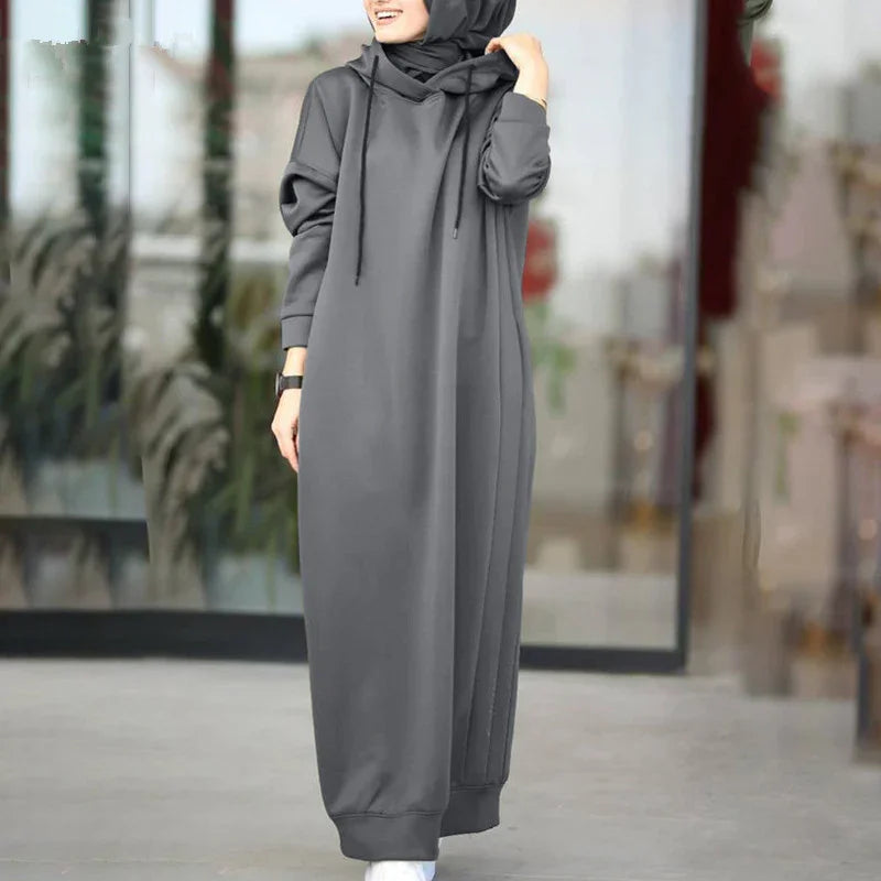 Woman wearing a long grey hooded abaya dress with a black hijab and white sneakers outdoors