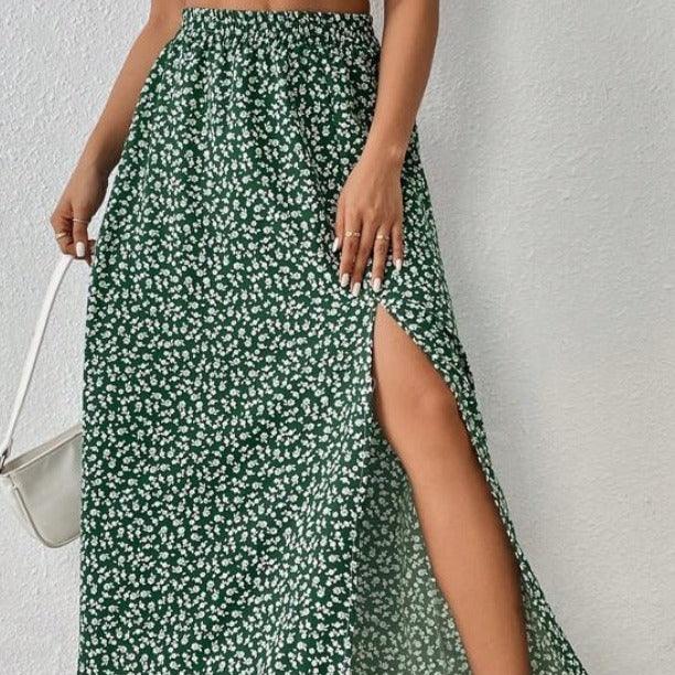 Woman wearing green floral midi skirt with side slit and elastic waistband, holding white handbag