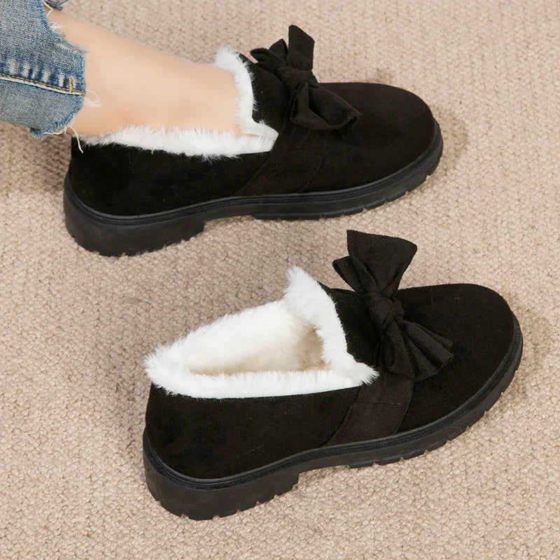 Black suede slip-on shoes with white fur lining and decorative bow, worn with frayed jeans