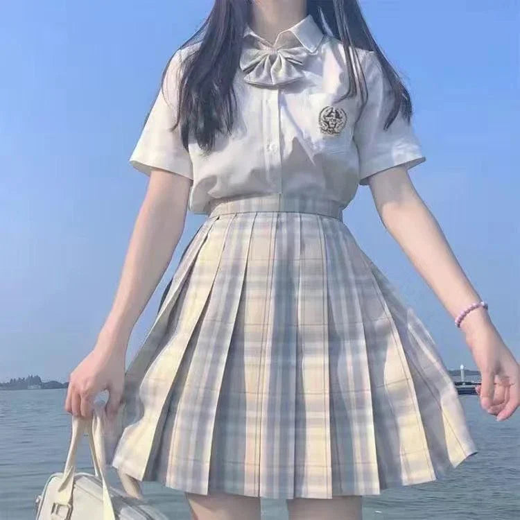Young woman wearing white blouse and pleated plaid skirt by the water under clear blue sky