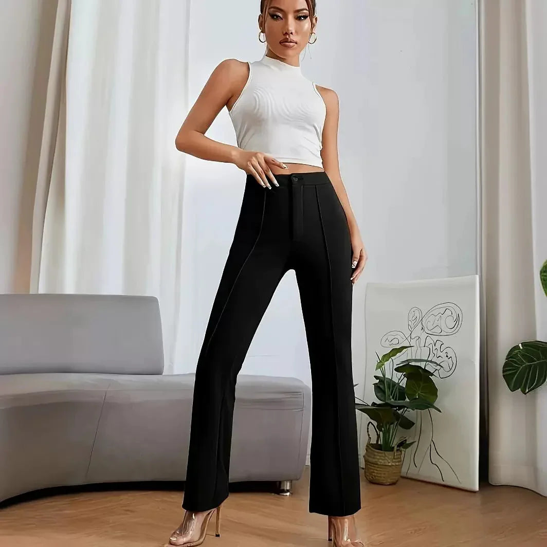Woman in white sleeveless top and black high-waist pants posing in modern living room