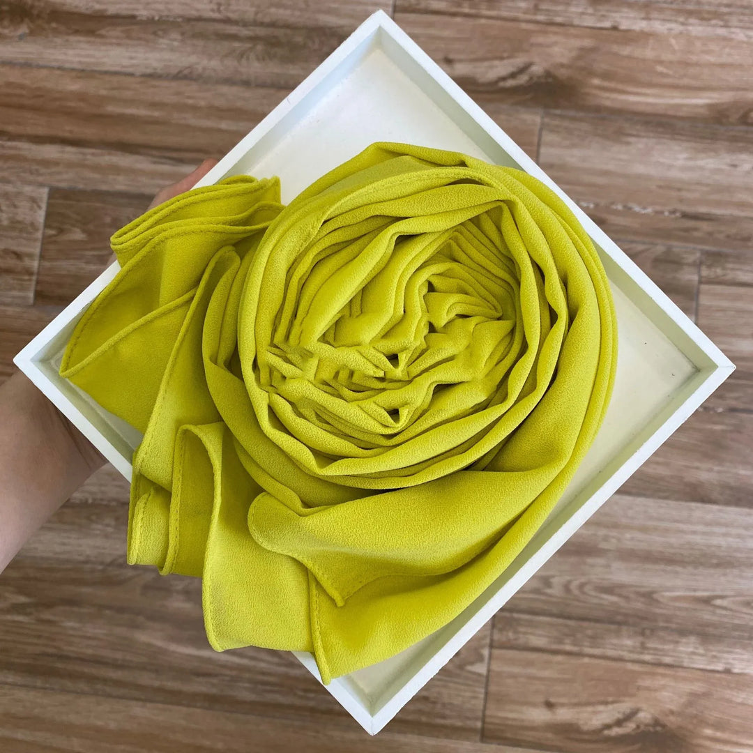 Hand holding a white square tray with a neatly rolled yellow fabric on wooden floor background