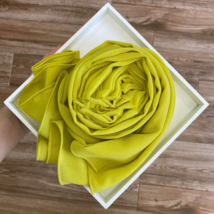 Hand holding a white square tray with a neatly rolled yellow fabric on wooden floor background