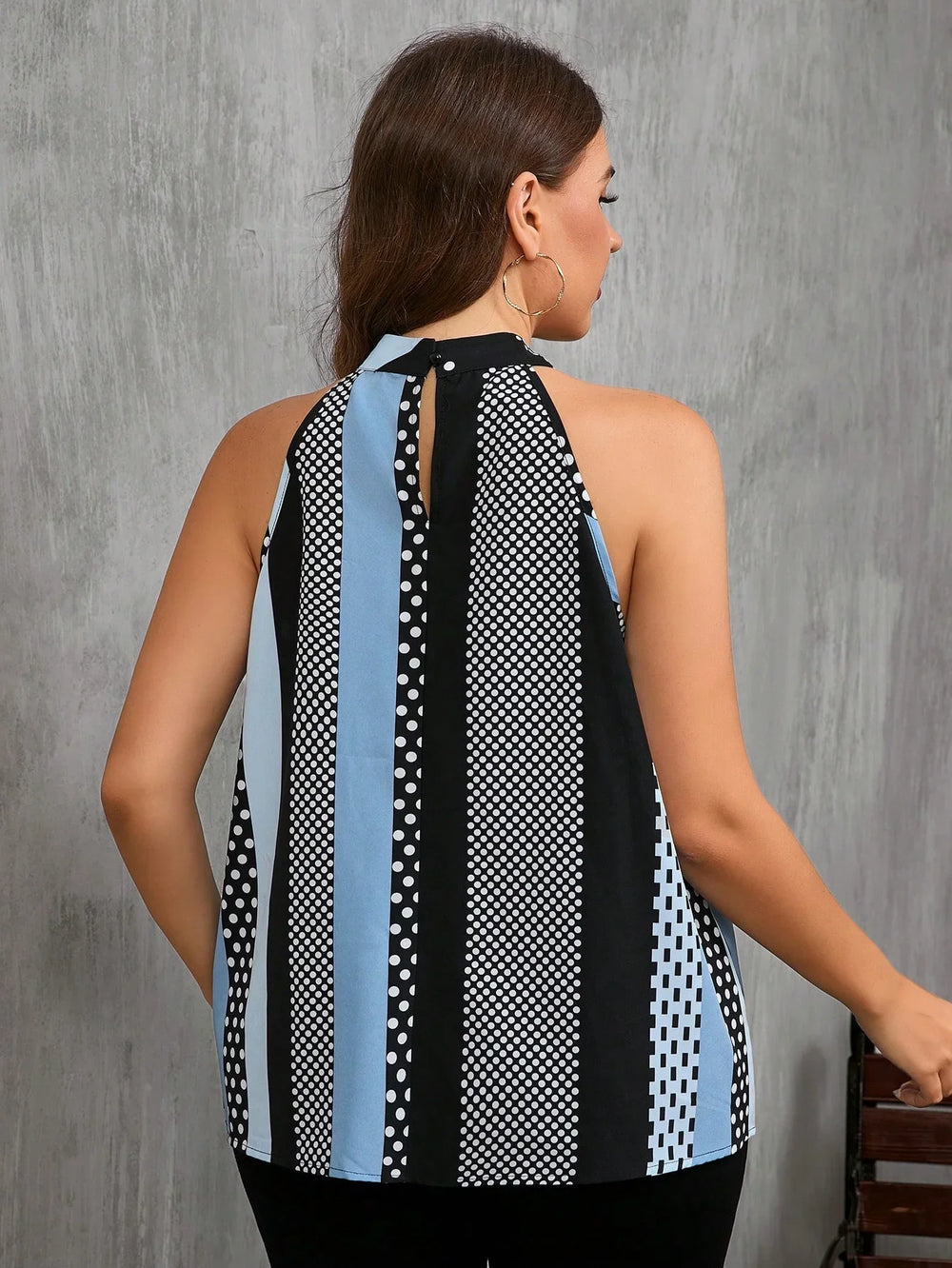 Woman wearing sleeveless halter neck top with blue, black, white vertical stripes and polka dot pattern