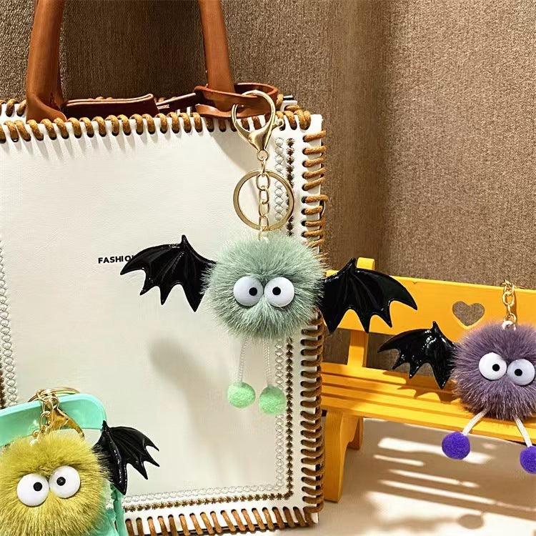 Furry bat keychains with big eyes and wings attached to bags and a yellow miniature bench