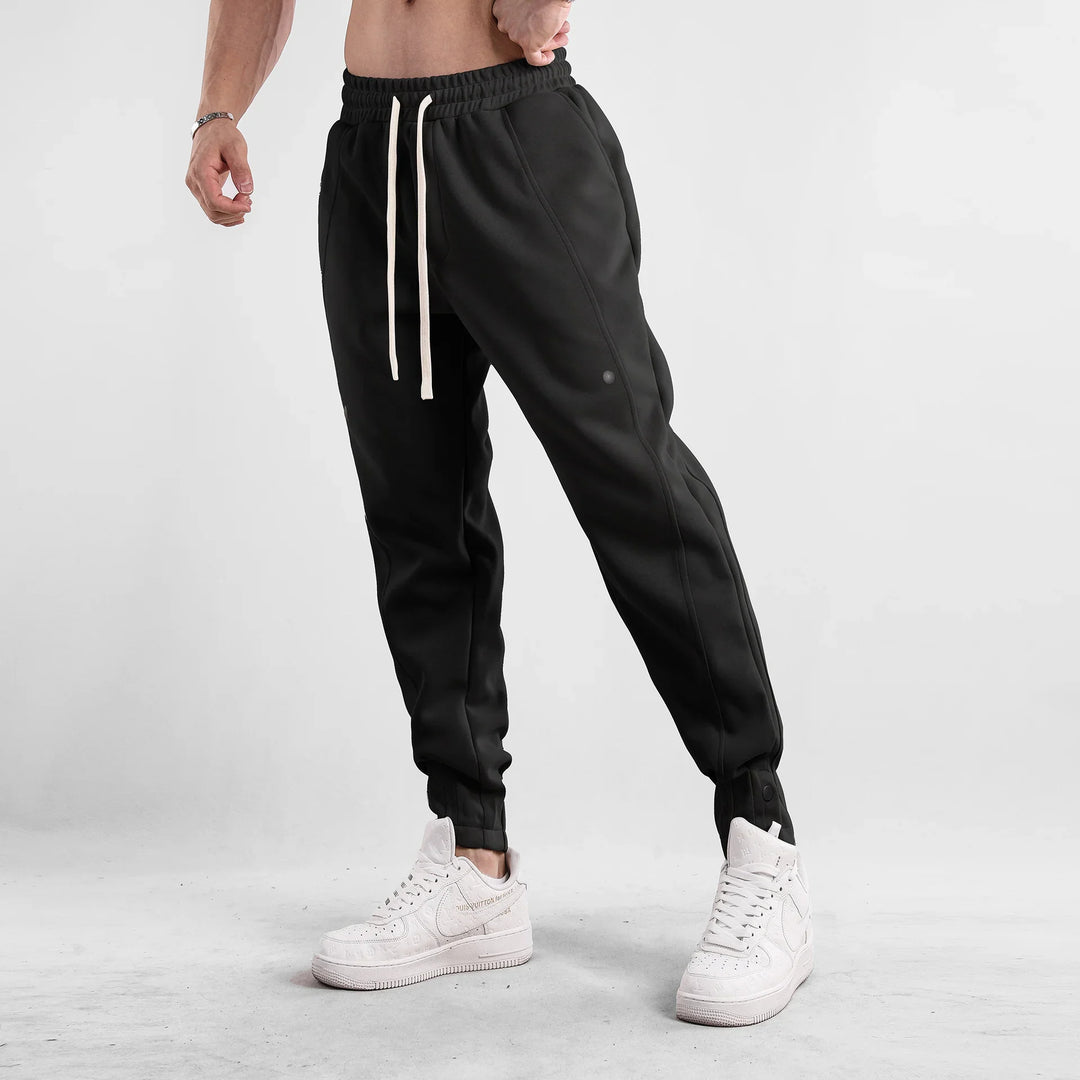 Male model wearing black jogger pants with white drawstrings and white high-top sneakers on gray background
