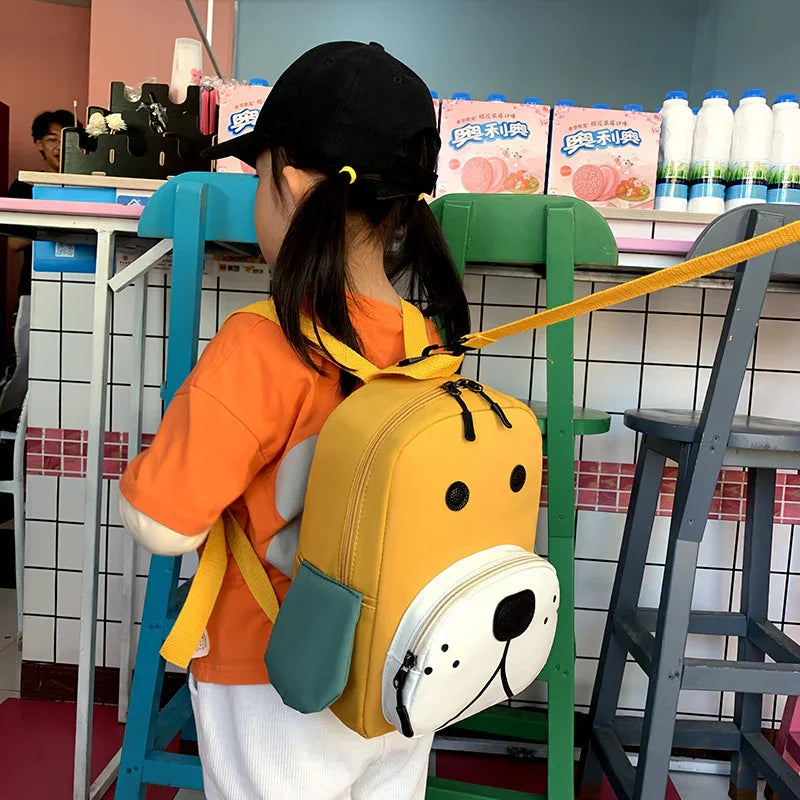 Child wearing black cap and orange shirt with yellow dog-shaped backpack in colorful cafe