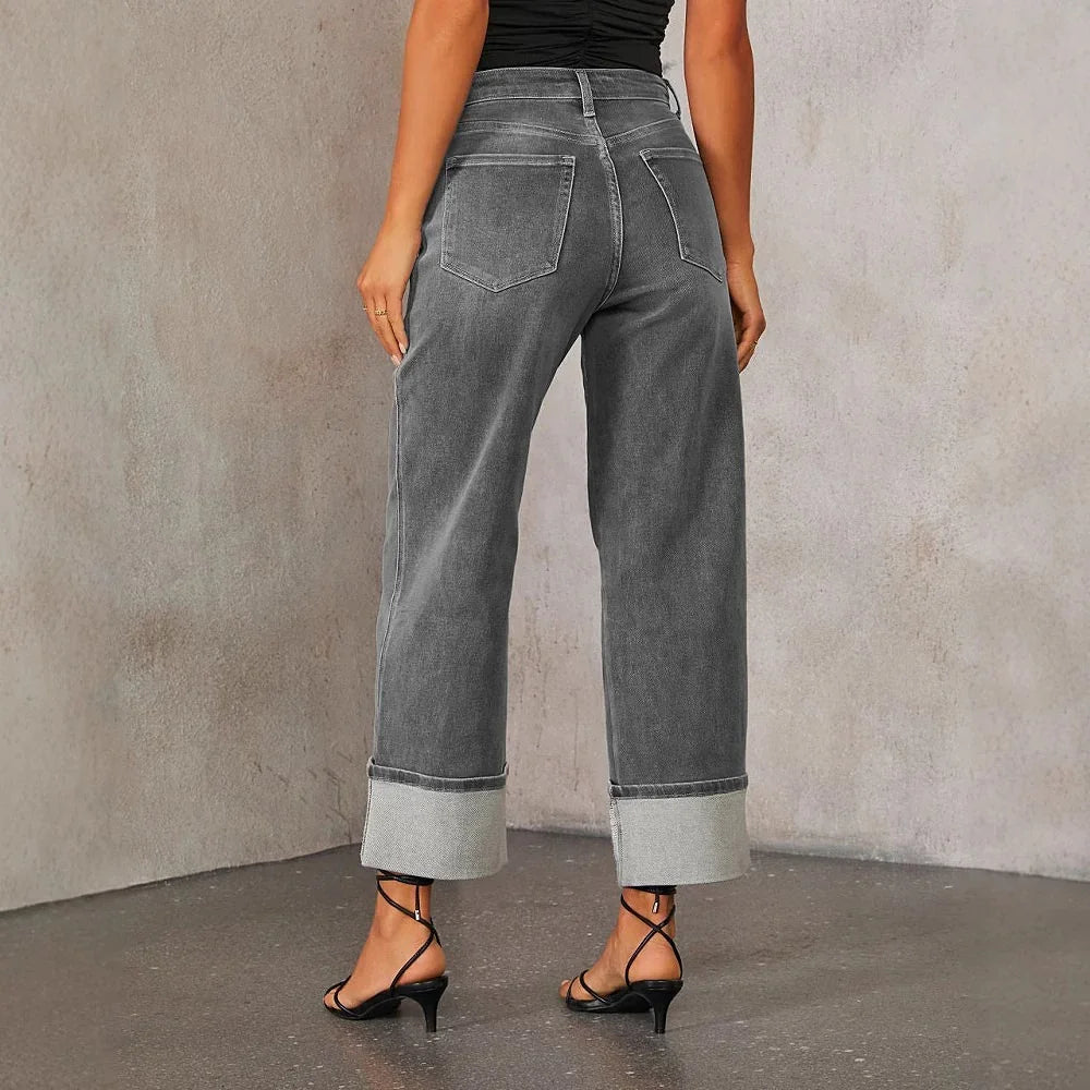 Back view of woman wearing high-waisted gray wide-leg jeans with cuffed hems and black strappy heels