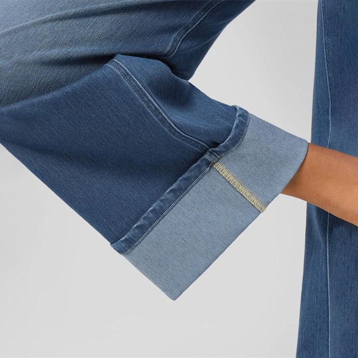 Close-up of a cuffed blue denim pant leg with visible stitching on a light gray background